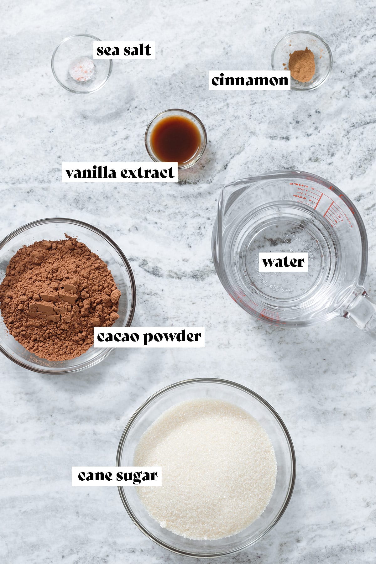 Cane sugar, cacao powder, water, and spices laid out on a grey stone background with text overlay.