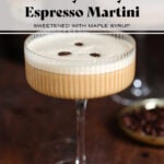 A beige-colored creamy espresso martini in a coupe martini glass garnished with three coffee beans on a dark wooden background.