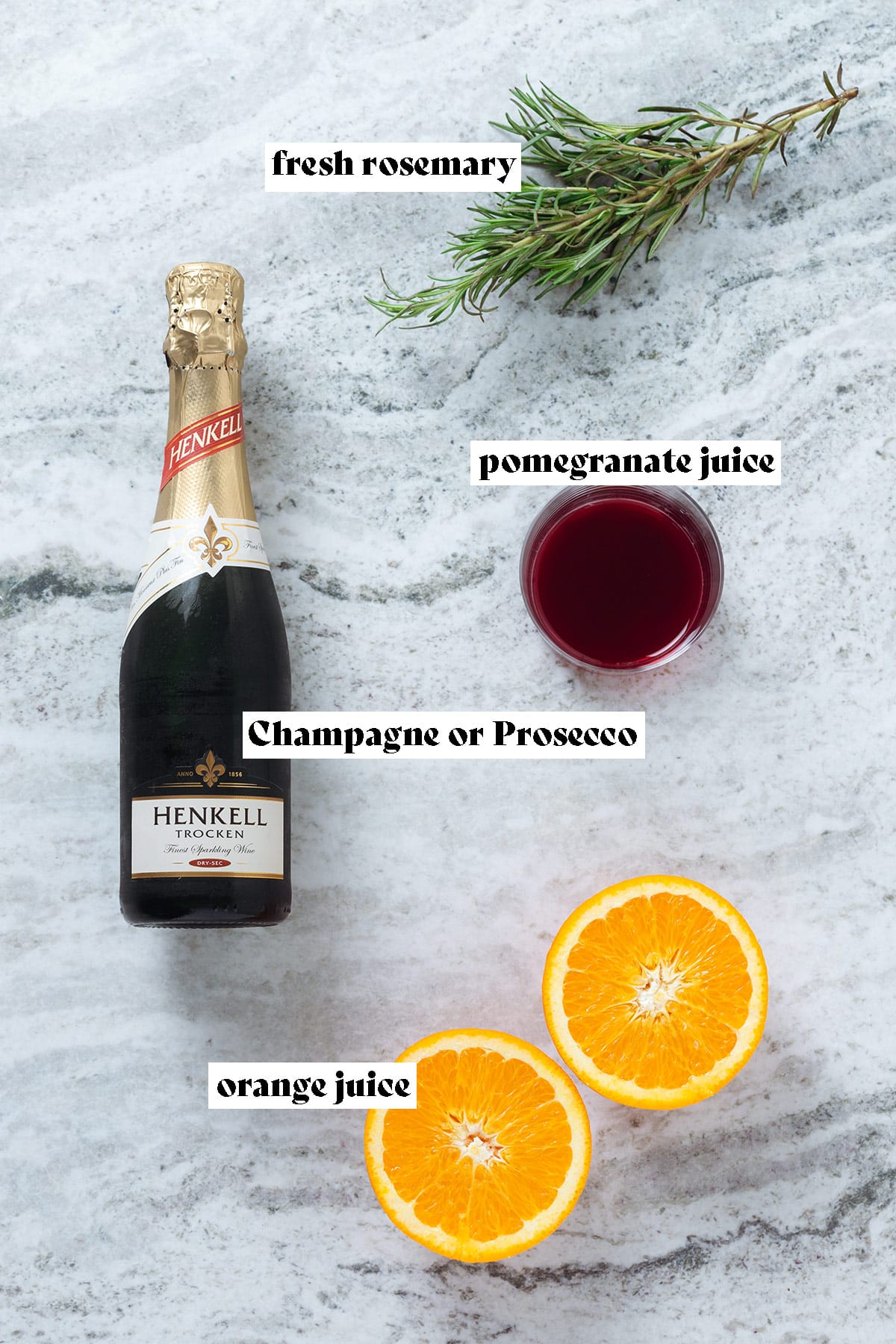 A bottle of prosecco, fresh rosemary, an orange, and pomegranate juice in a glass on a grey stone background with text overlay.