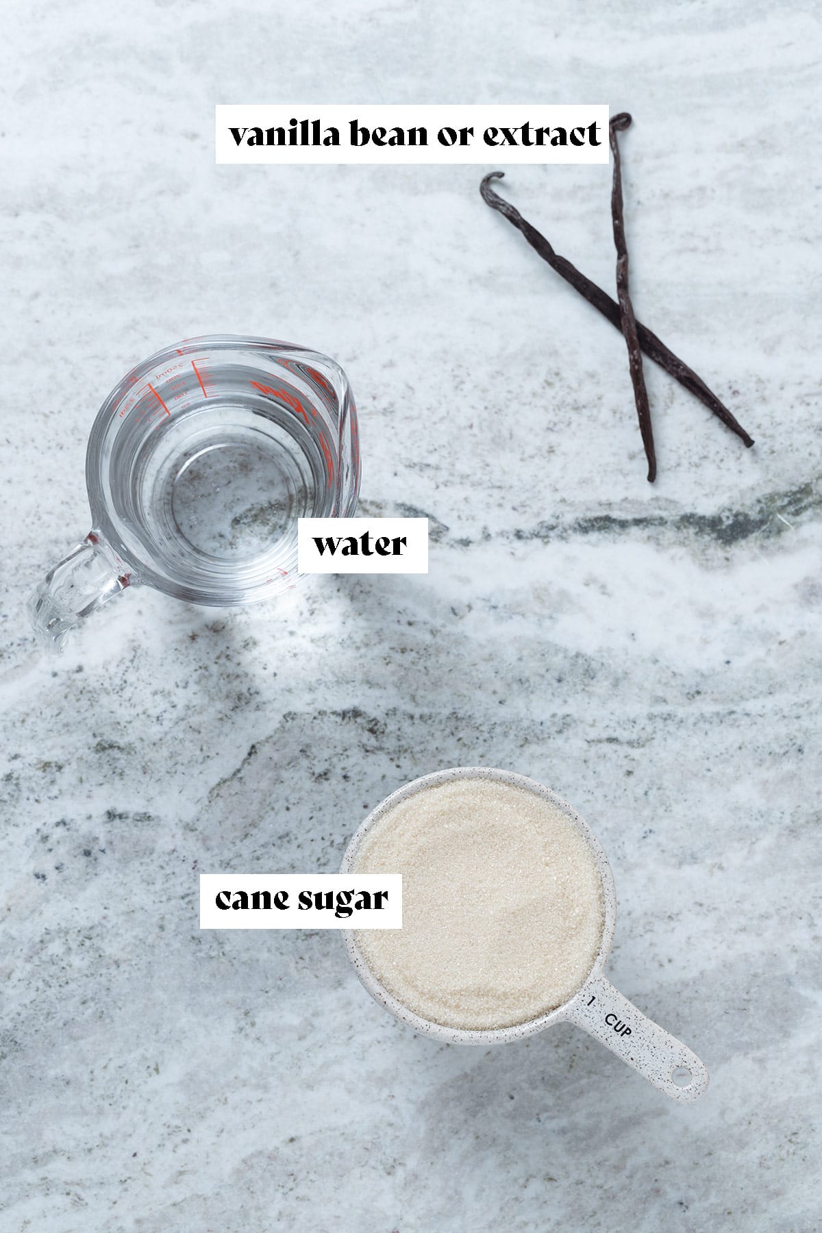 Cane sugar, water, and a whole vanilla bean on a grey stone background with text overlay.