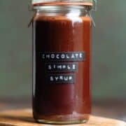 Chocolate syrup in a glass jar with a black and white embossed label on a dark wooden background.