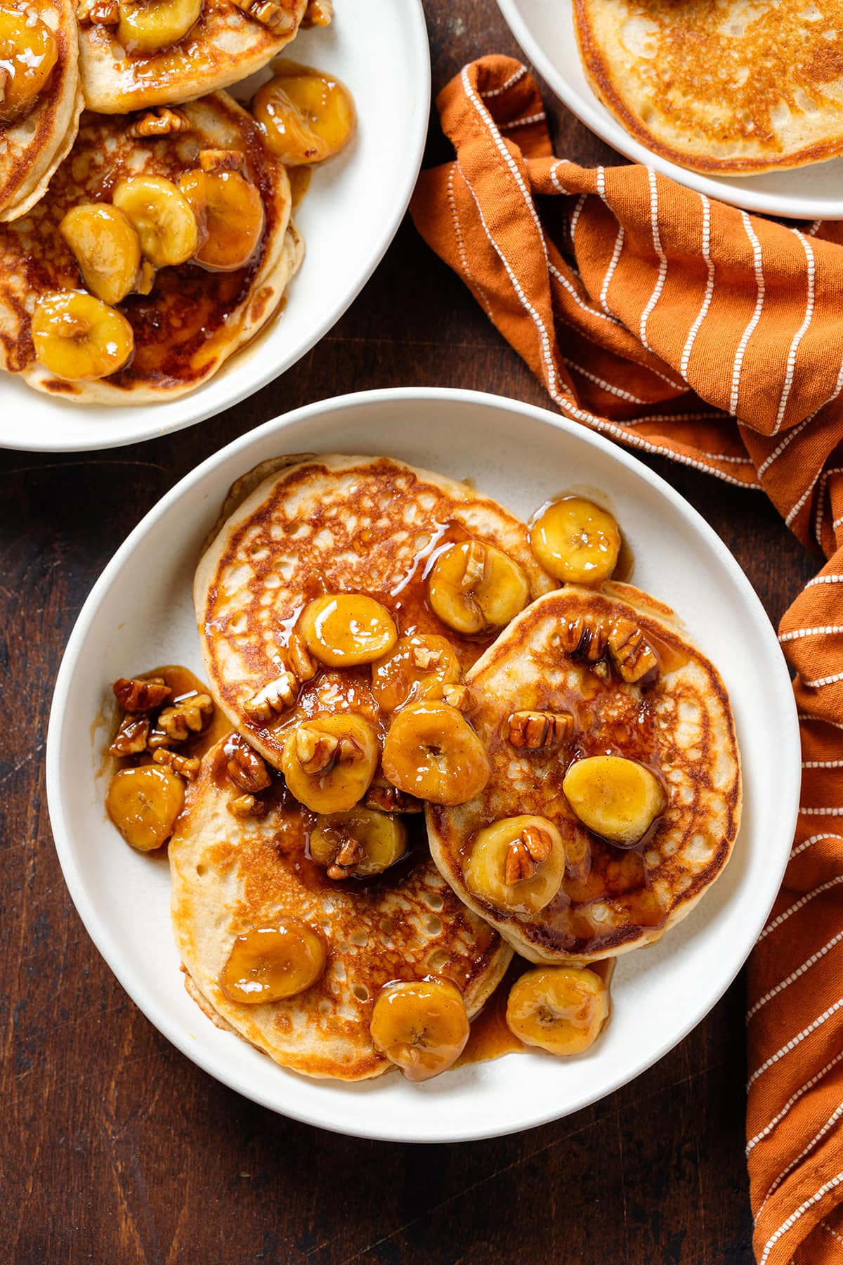 Three pancakes on a white plate topped with caramelized bananas and pecans.