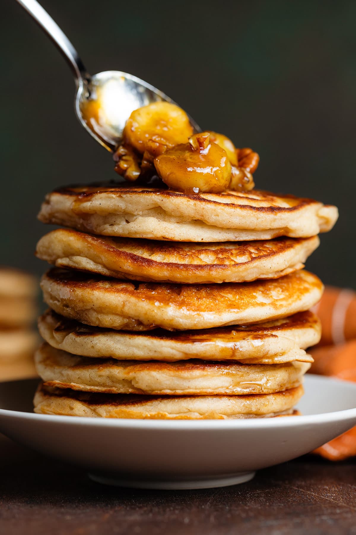 A stack of pancakes being topped with caramelized bananas.