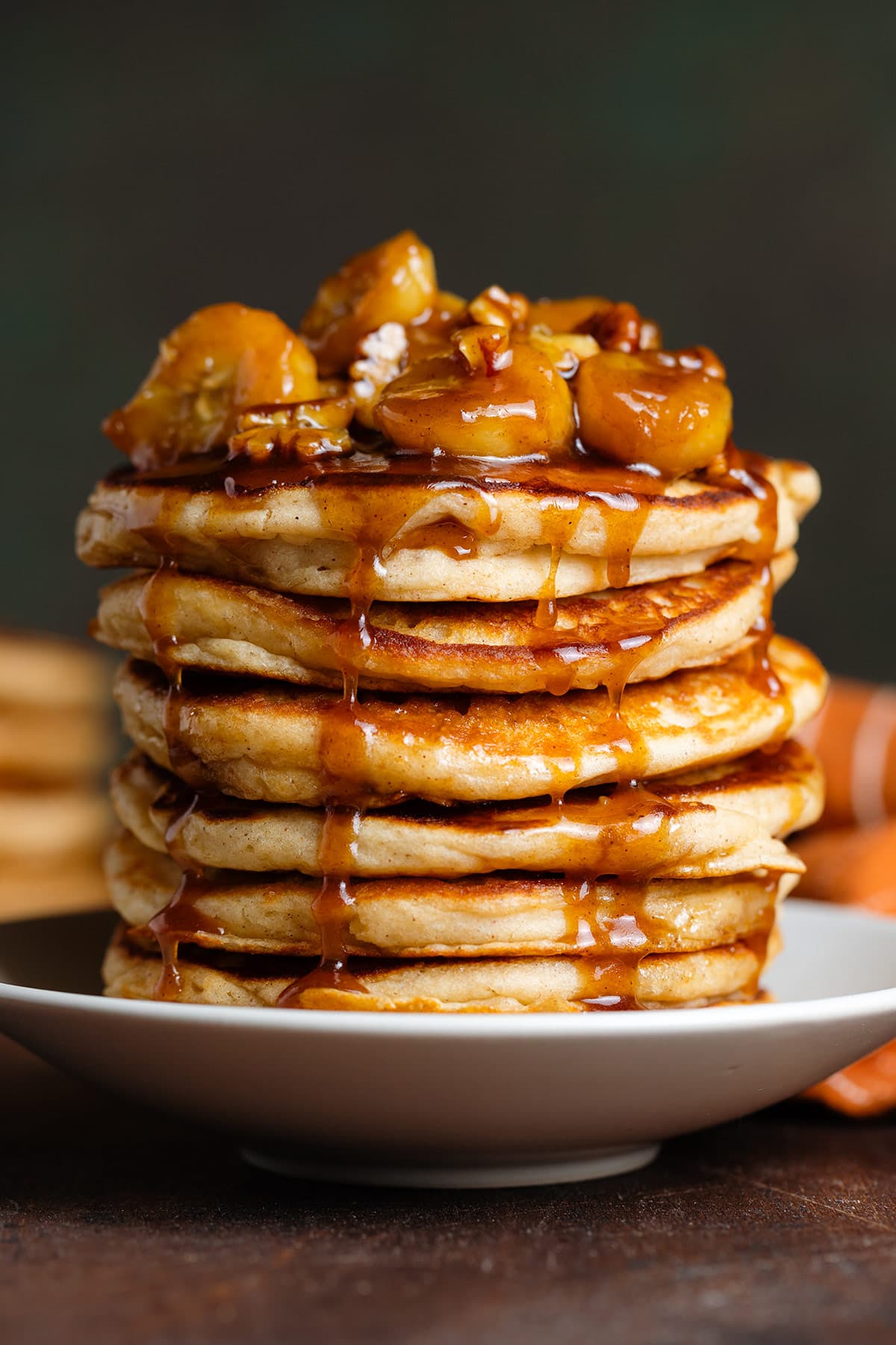 A stack of pancakes with caramelized bananas and pecans with caramel sauce dripping down the sides.