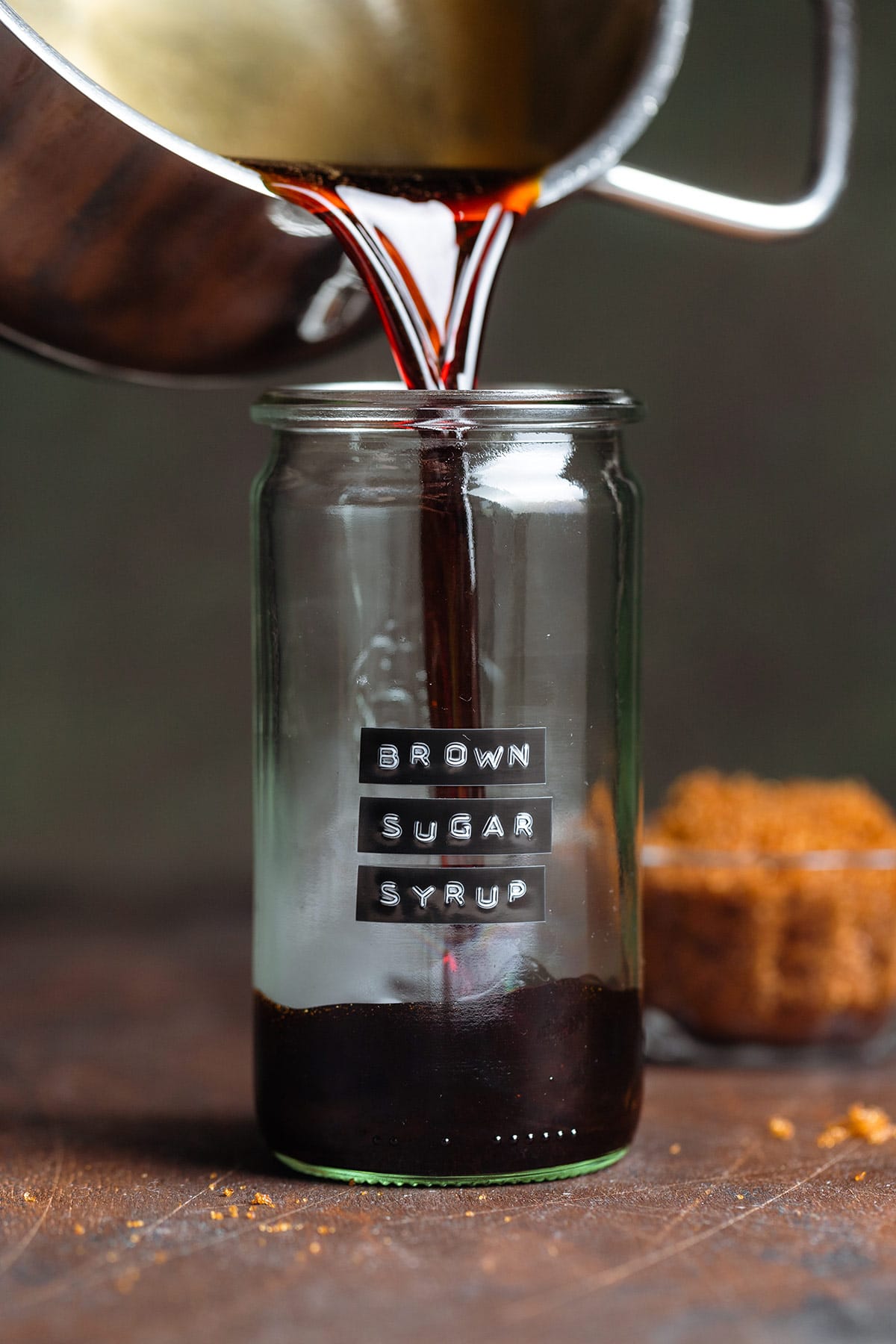 Dark brown sugar syrup being poured into a glass jar.
