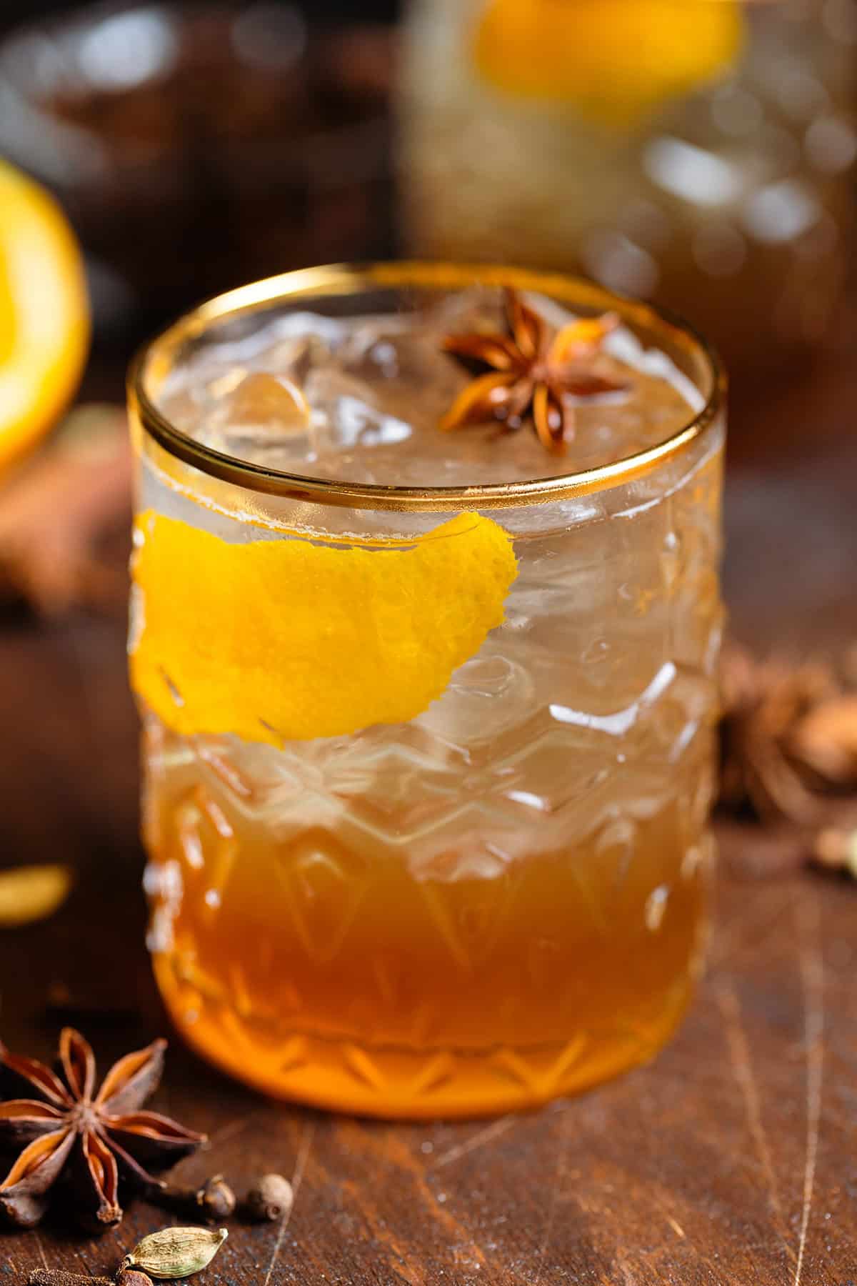 Old fashioned cocktail in a gold-rimmed glass with ice, orange zest, and star anise.