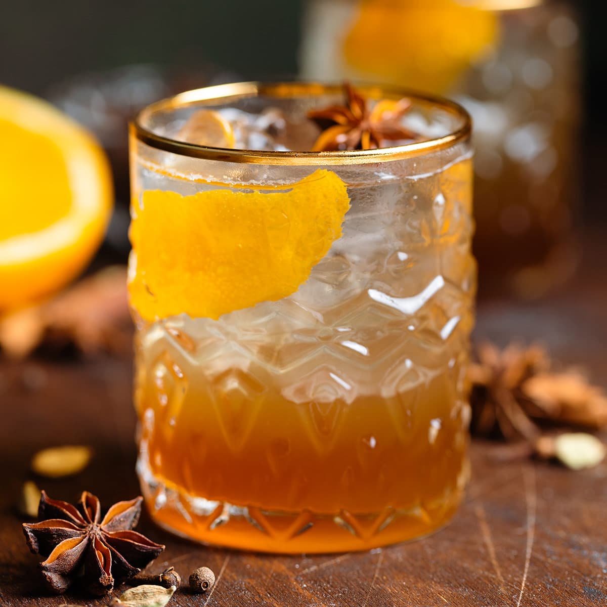 Old fashioned cocktail in a gold-rimmed glass with ice, orange zest, and star anise.