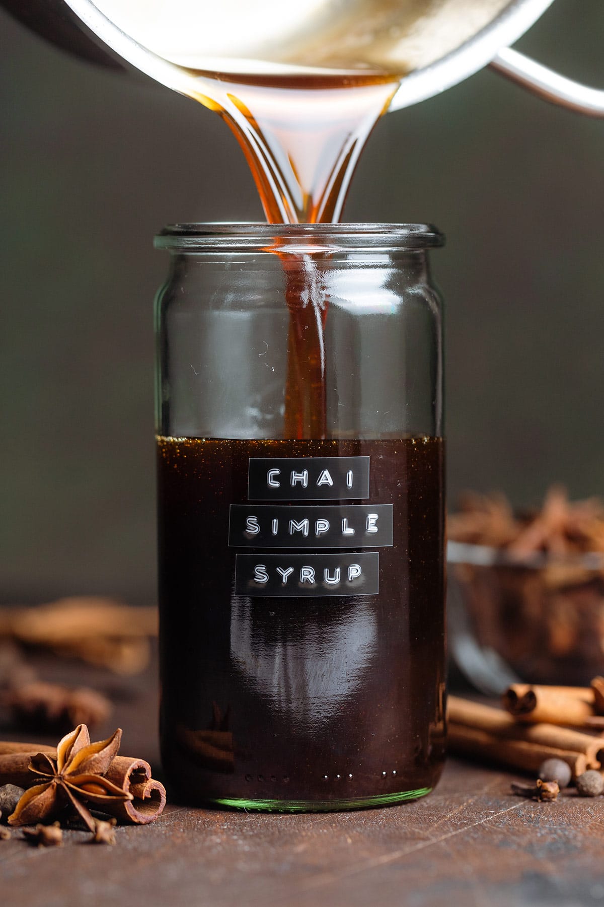 Dark syrup being poured into a glass jar with embossed label that says chai simple syrup.