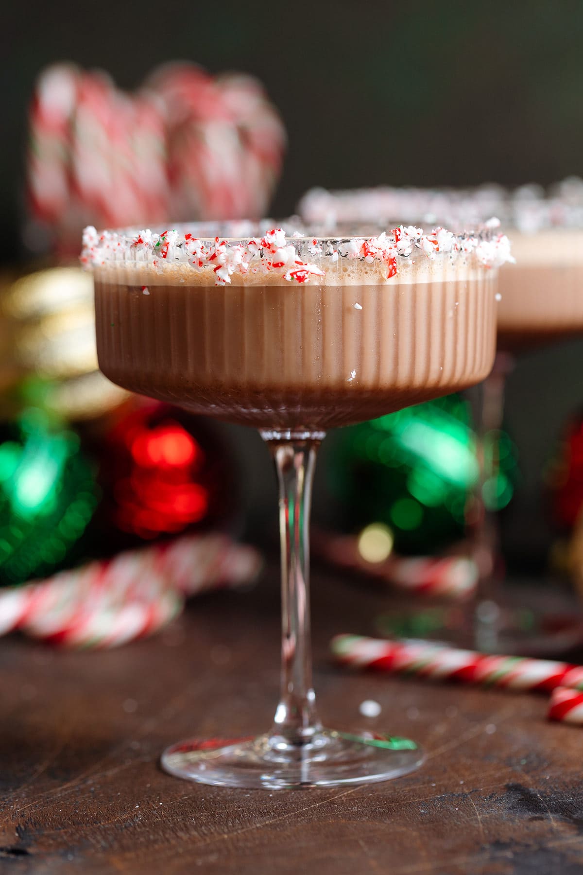 A coupe glass with creamy espresso martini garnished with crushed candy canes on the rim and three coffee beans on top.