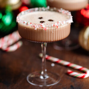 A coupe glass with creamy espresso martini garnished with crushed candy canes on the rim and three coffee beans on top.