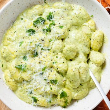 Creamy green pesto gnocchi in a low bowl garnished with fresh parsley, lemon zest, pecorino, and black pepper.