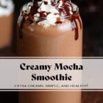 A dark brown mocha smoothie in a tall glass garnished with whipped cream and chocolate sauce on a dark wooden background.