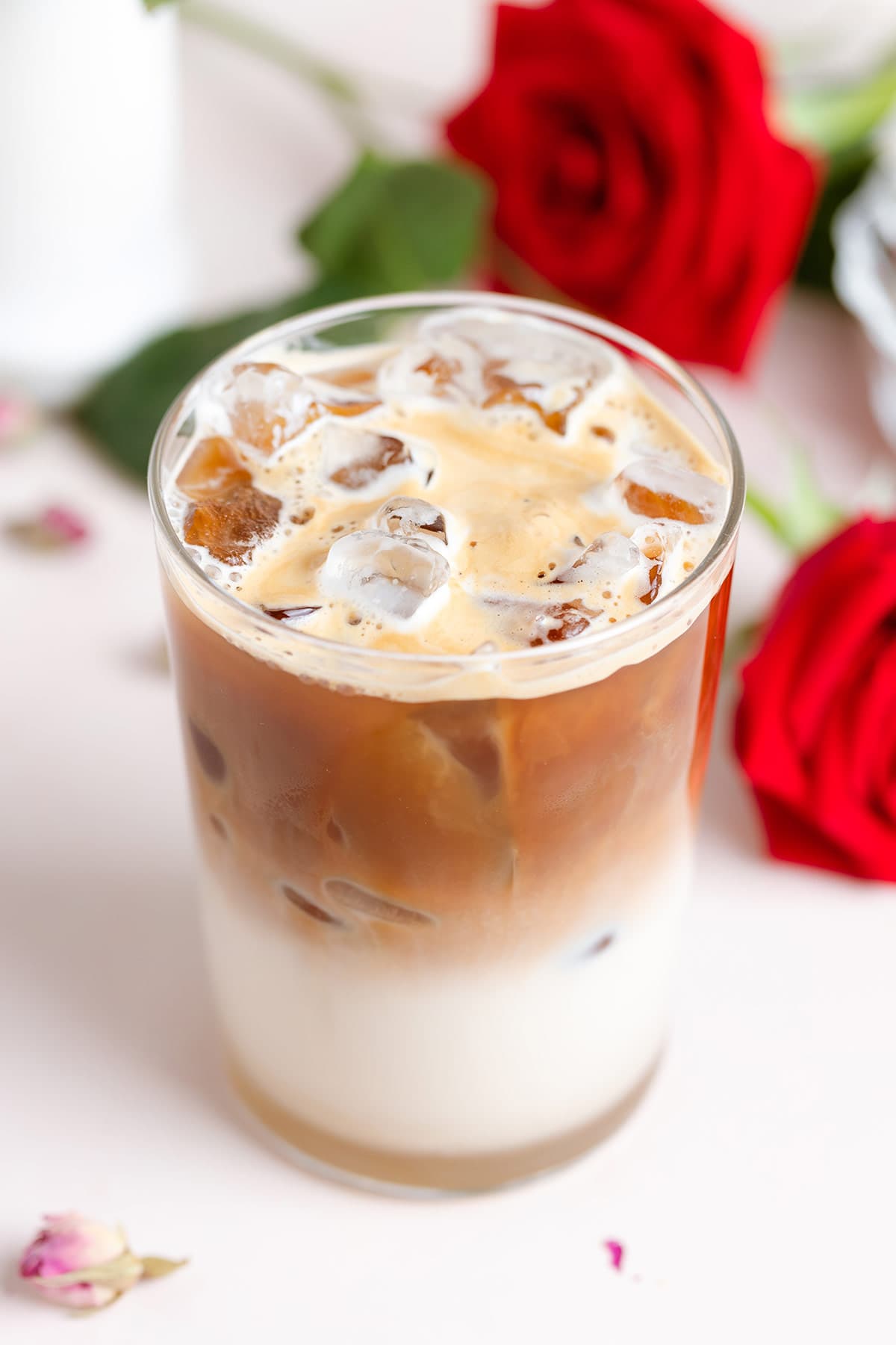 A tall glass with ice and milk on the bottom and fresh espresso poured on top.