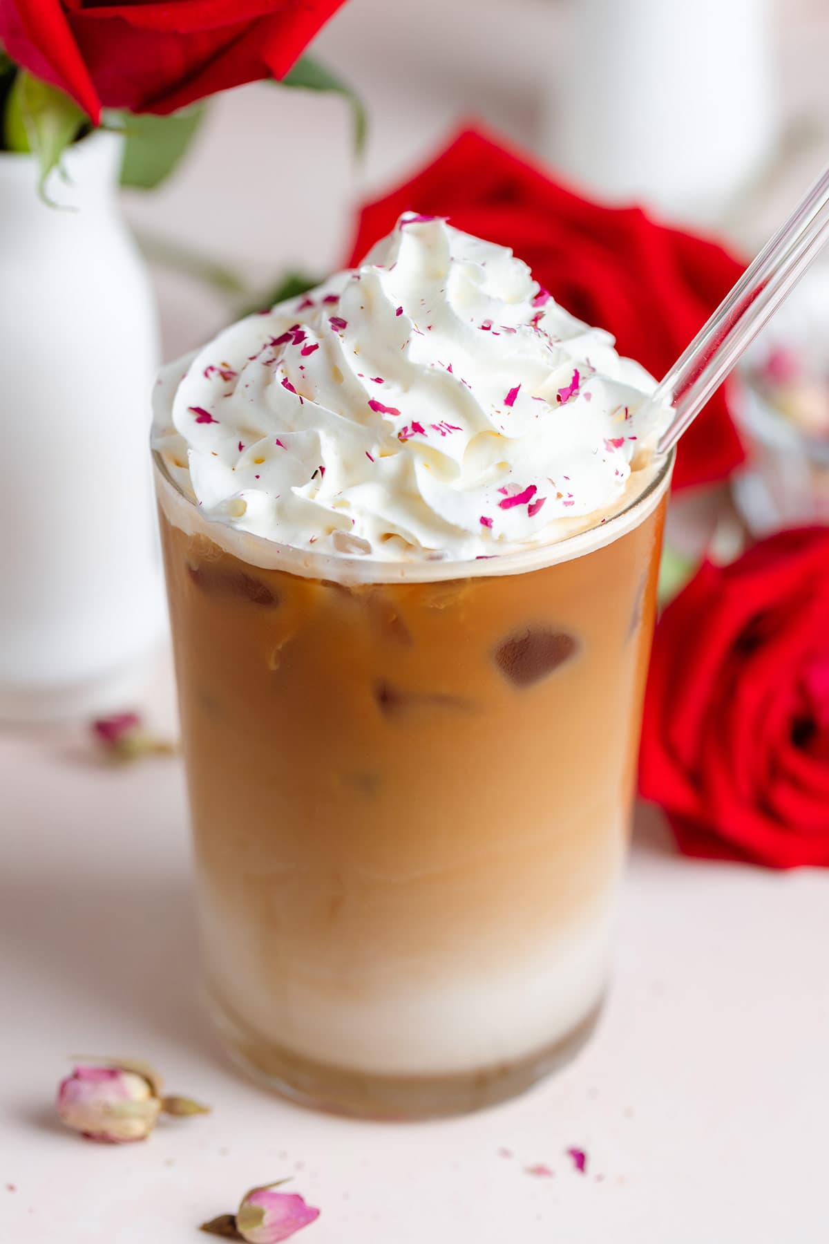 Iced latte with whipped cream and crushed dried rose petals sprinkled on top with a glass straw.
