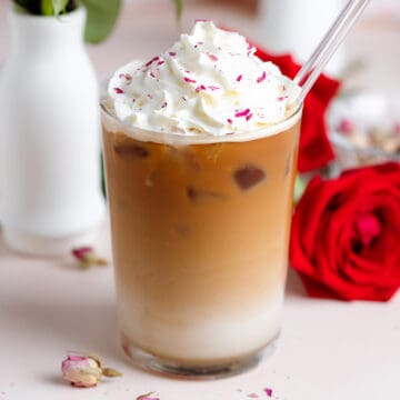 Iced latte with whipped cream and crushed dried rose petals sprinkled on top with a glass straw.