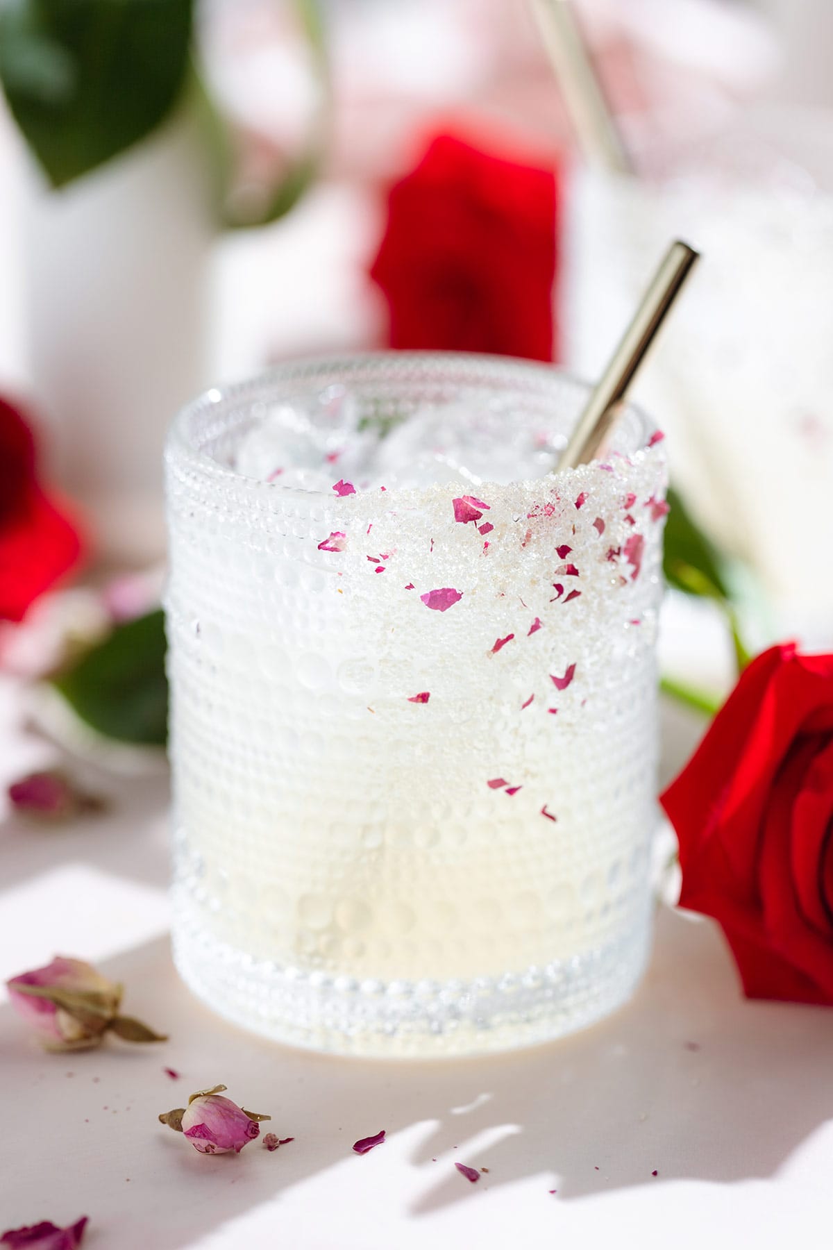 A margarita cocktail in a short glass garnished with a sugar rim with crushed dried rose petals and a gold straw.