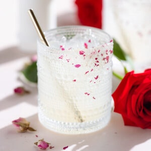 A margarita cocktail in a short glass garnished with a sugar rim with crushed dried rose petals and a gold straw.