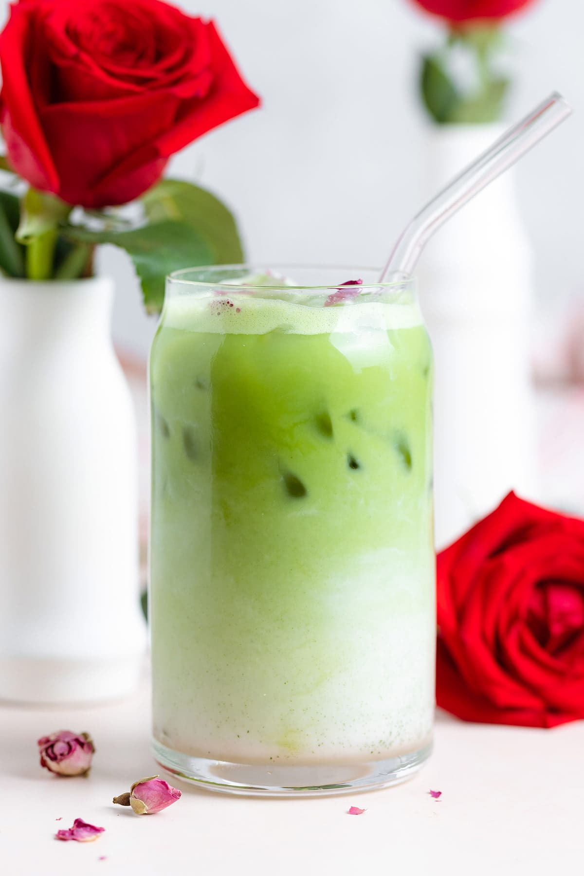 Green matcha latte in a tall glass with a glass straw with red roses around the glass.