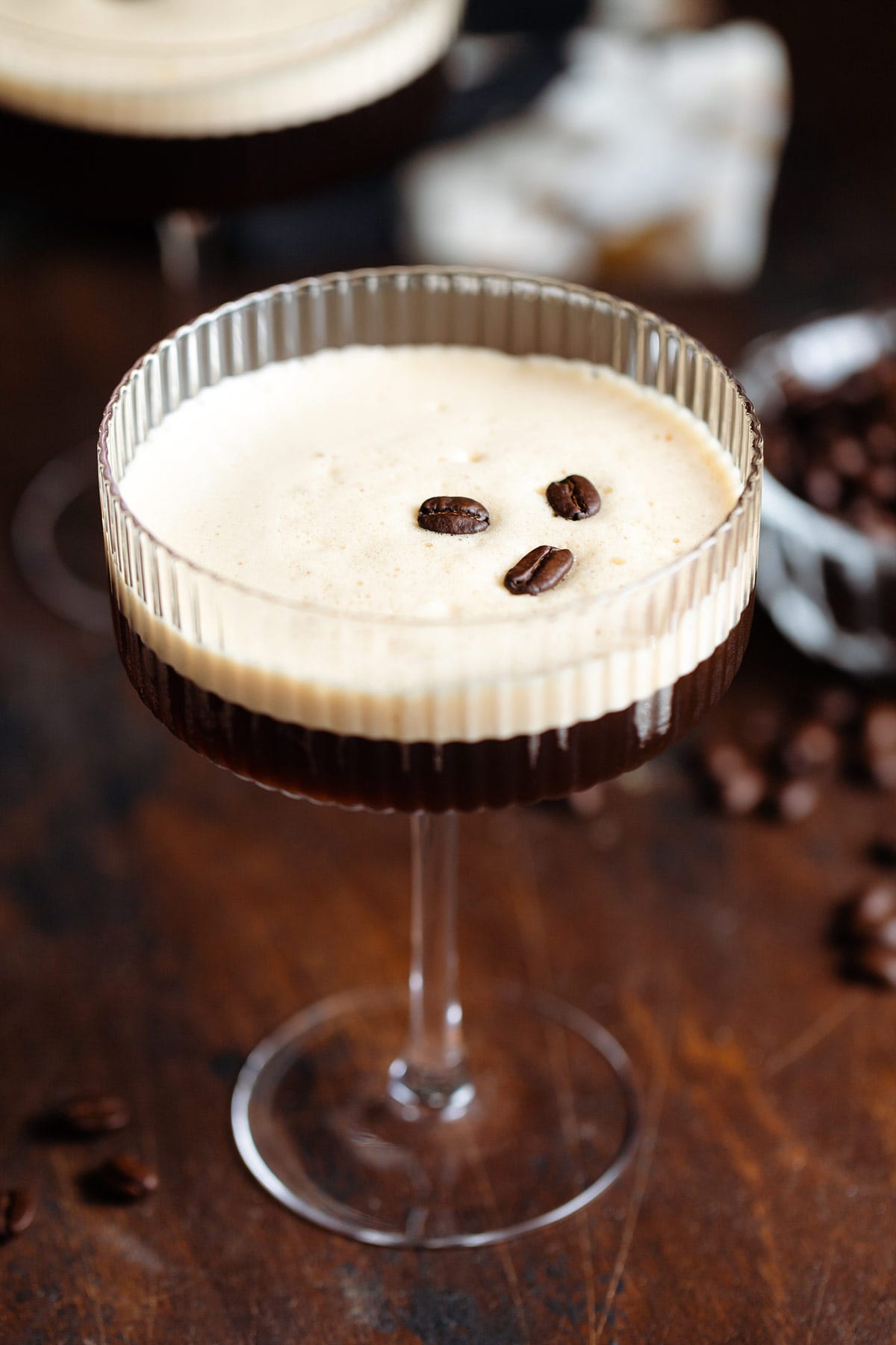 Espresso martini in a coupe glass with a layer of foam on top garnished with three coffee beans.