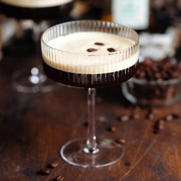 Espresso martini in a coupe glass with a layer of foam on top garnished with three coffee beans.