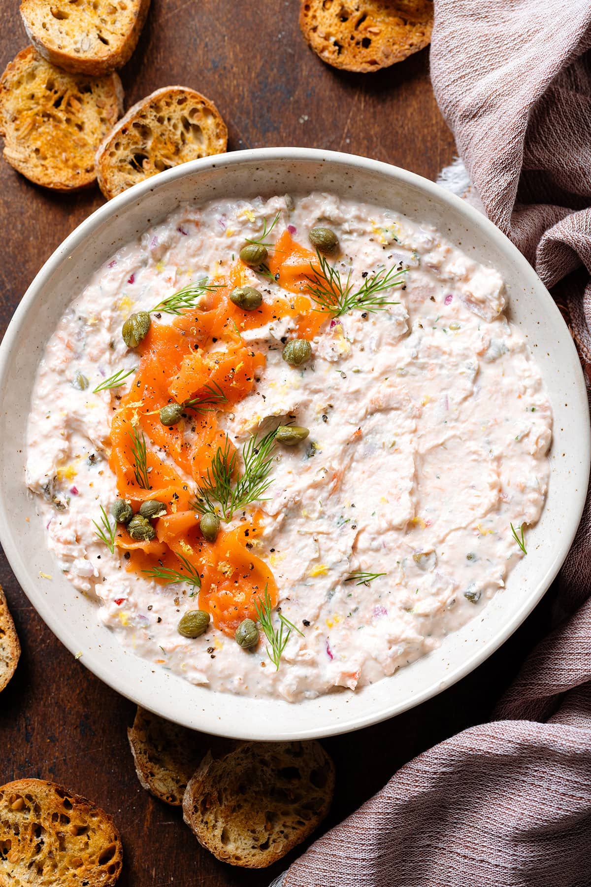 Smoked salmon dip garnished with more smoked salmon, capers, and fresh dill in a white bowl.