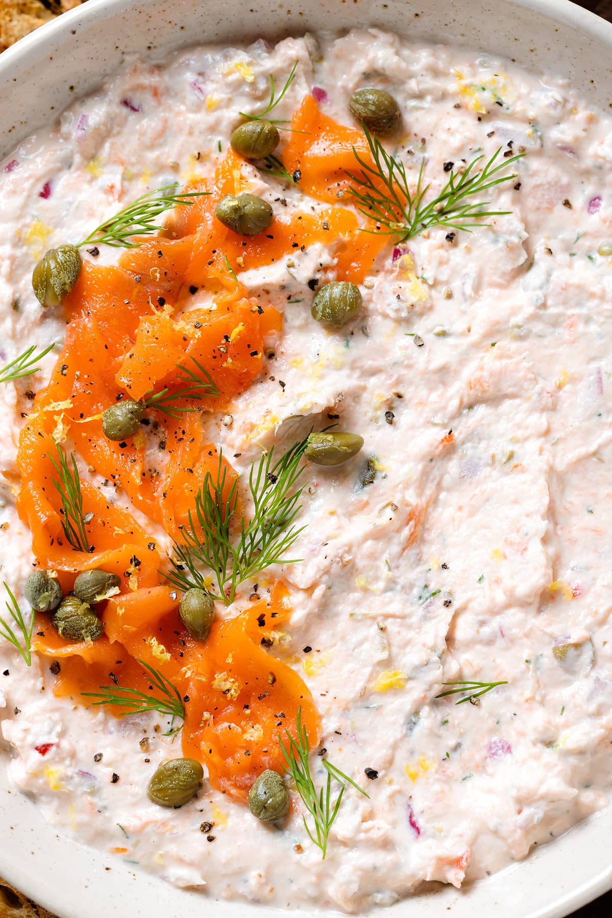 Smoked salmon dip garnished with more smoked salmon, capers, and fresh dill in a white bowl.