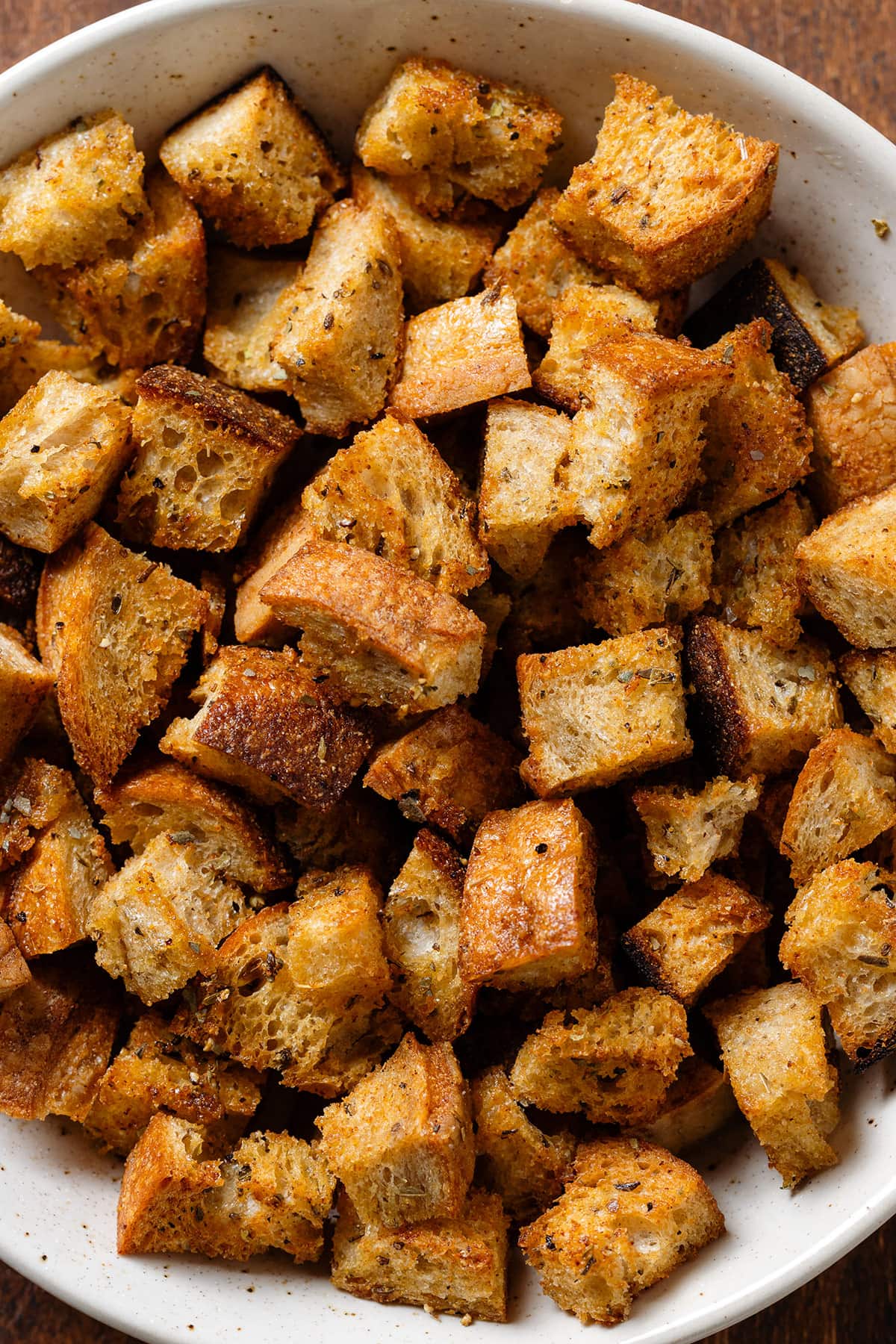 Golden brown sourdough croutons in a white bowl on a wooden background.