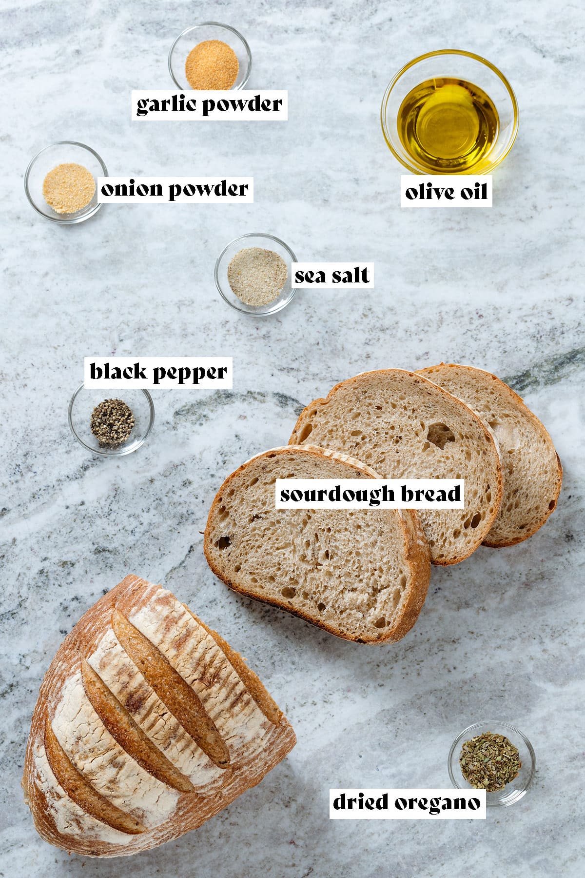A loaf of bread, olive oil, garlic powder, onion powder, and oregano all measured and laid out with text overlay.