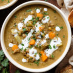 Lentil soup with carrots, celery and potatoes in a white bowl garnished with yogurt and chopped fresh parsley.