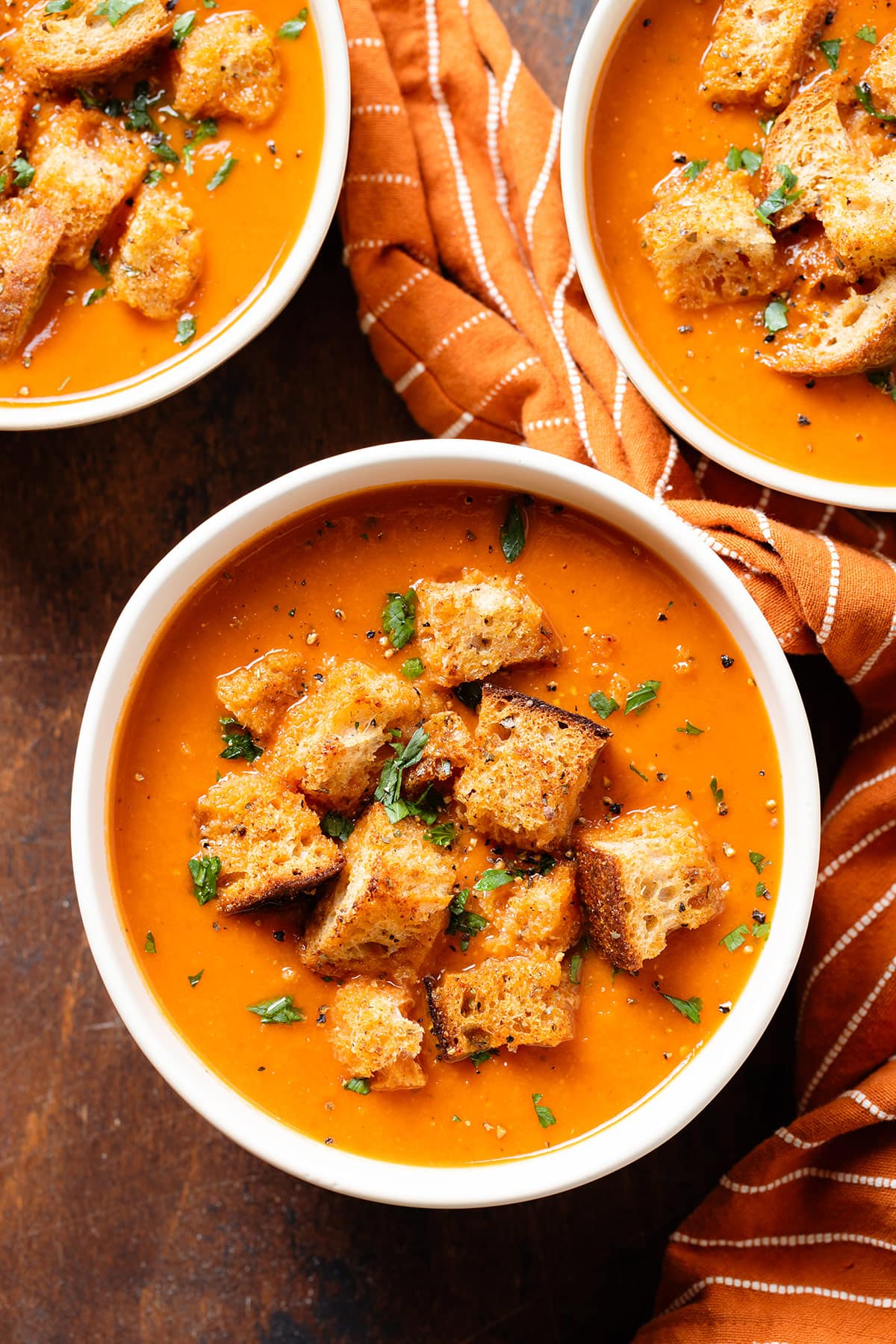 Tomato soup in white bowls topped with croutons, fresh parsley, and black pepper.