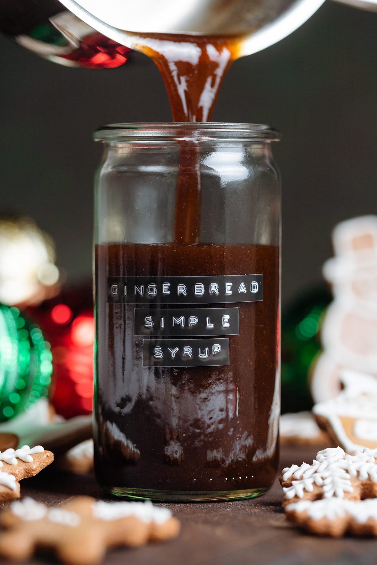 Dark brown syrup being poured into a glass jar with an embossed gingerbread simple syrup label.