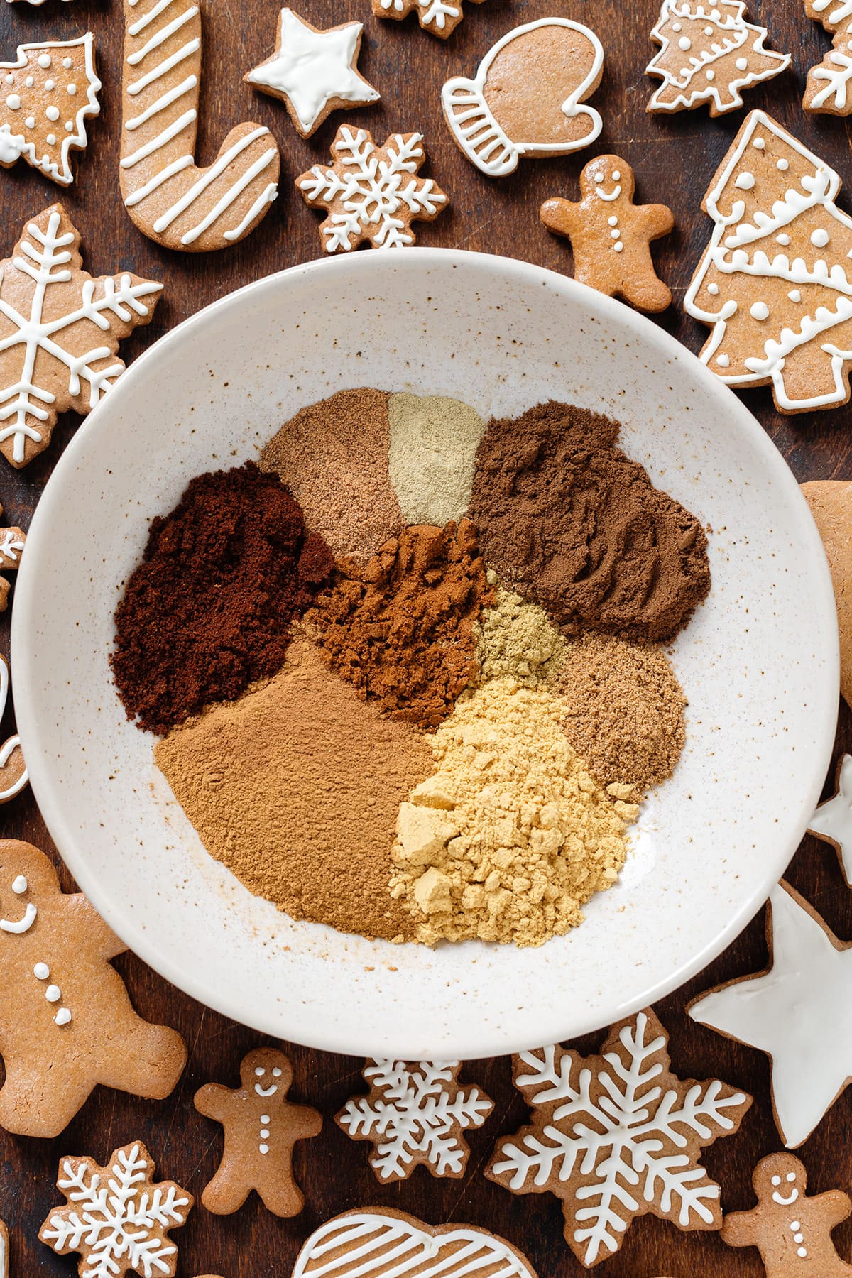 Various spices all measured out and separated in a low bowl with gingerbread cookies around it.