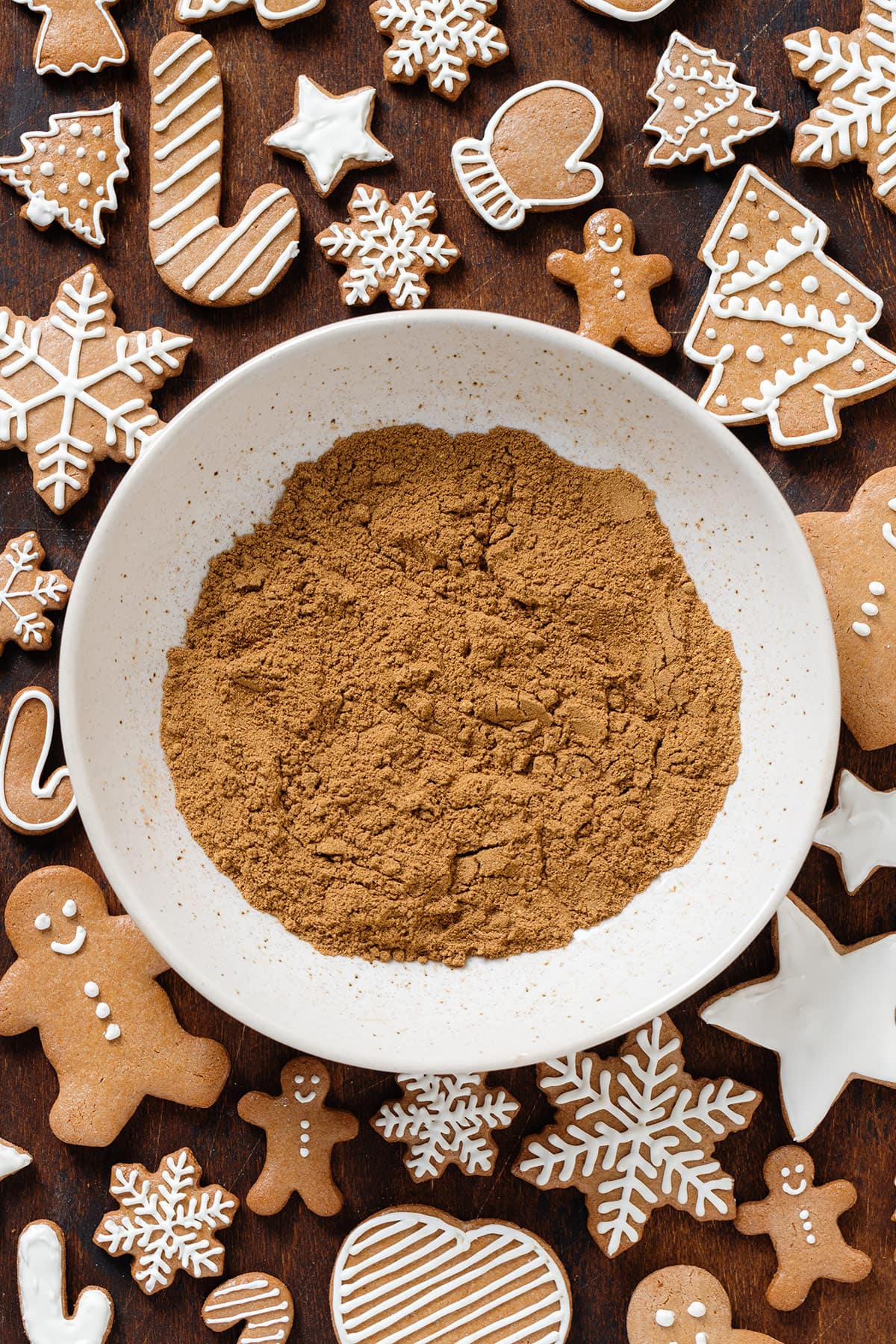 Gingerbread spice in a beige low bowl with gingerbread cookies all around it.