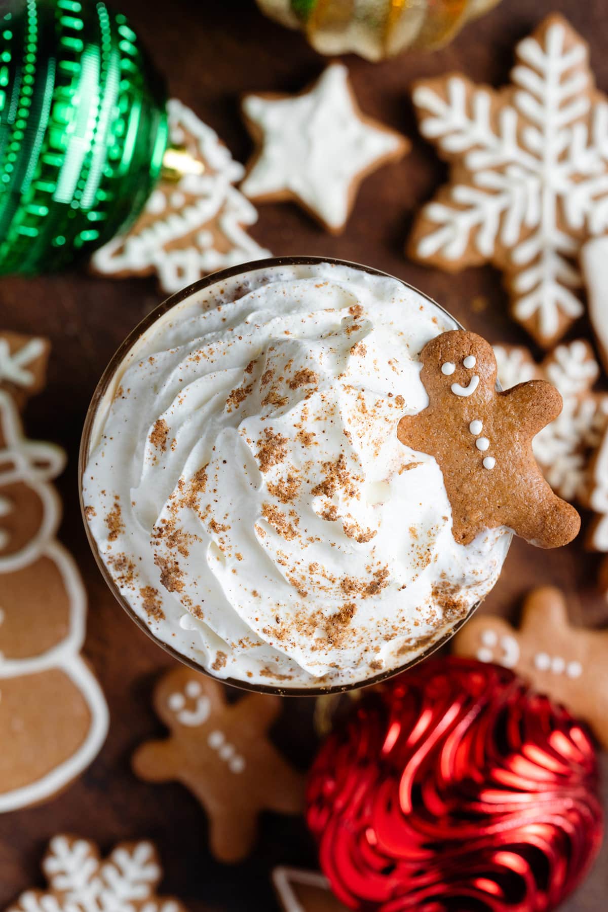 A glass with iced latte topped with a generous amount of whipped cream, gingerbread spice, and a small gingerbread cookie.
