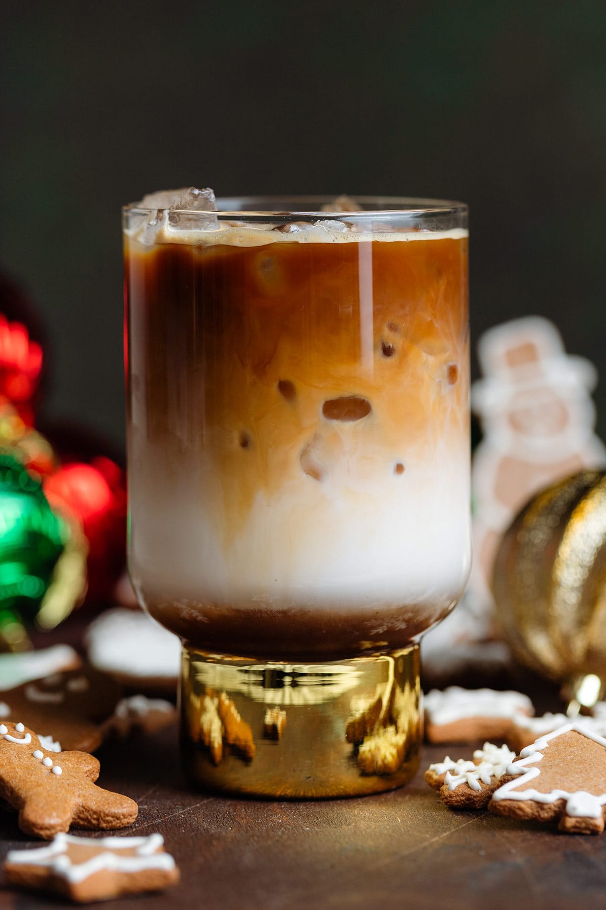 An iced latte with in a tall glass with a gold bottom, with three layers of syrup, milk, and espresso on top.