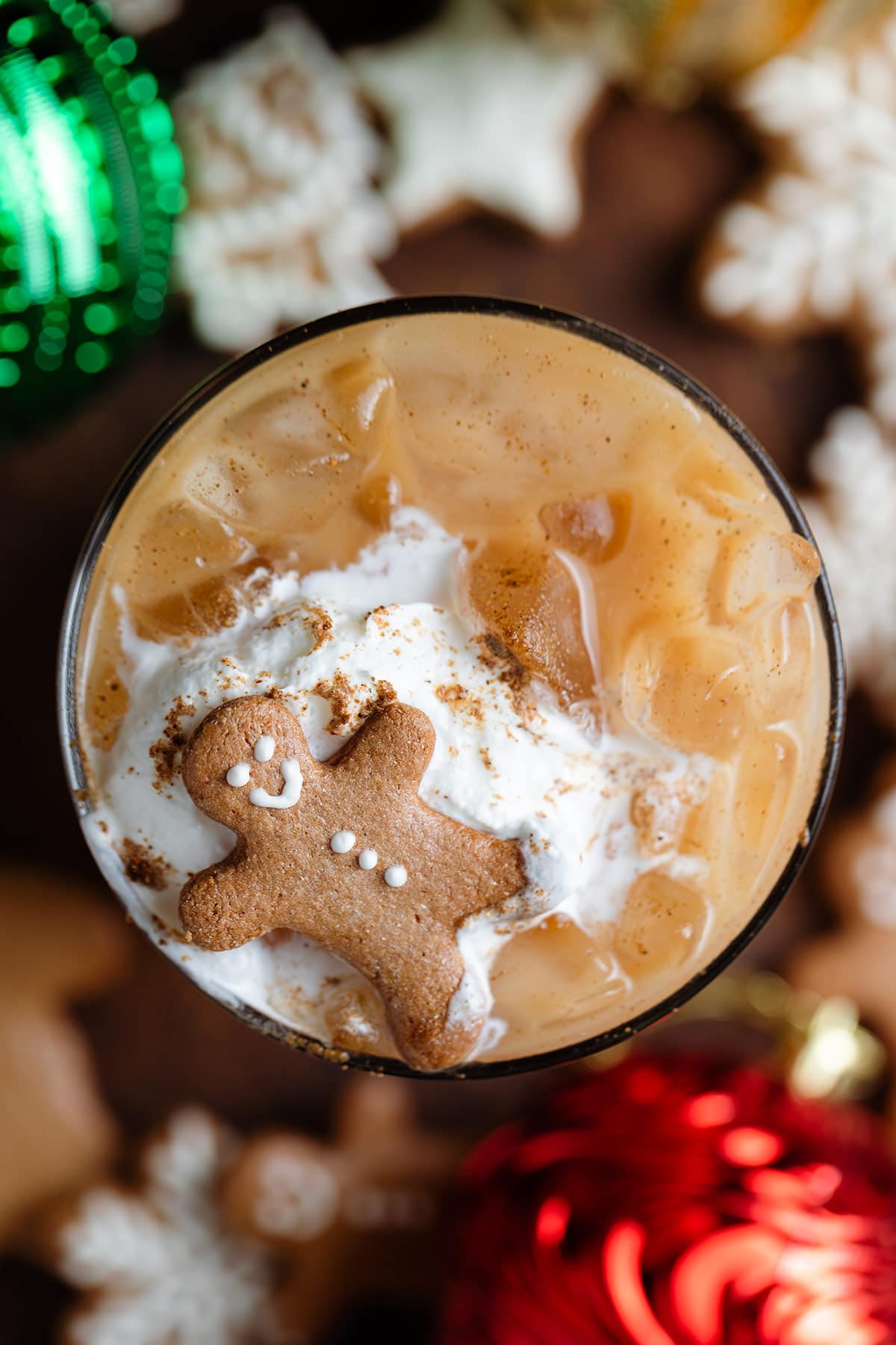 Iced chai latte in a tall glass topped with a dollop of whipped cream, gingerbread spice, and a small gingerbread man.