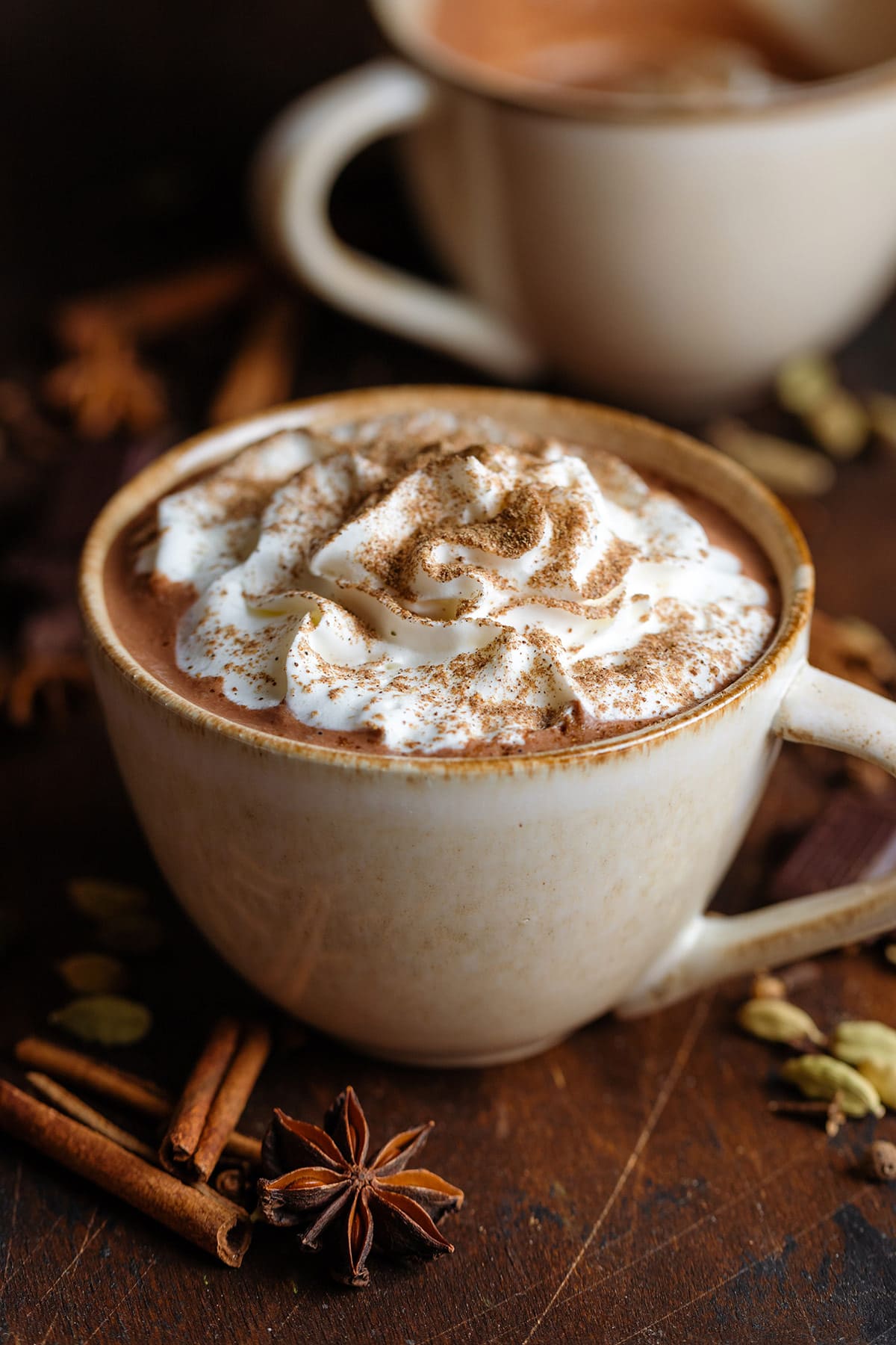 Creamy hot chocolate with whipped cream and chai spice on top in a beige mug.