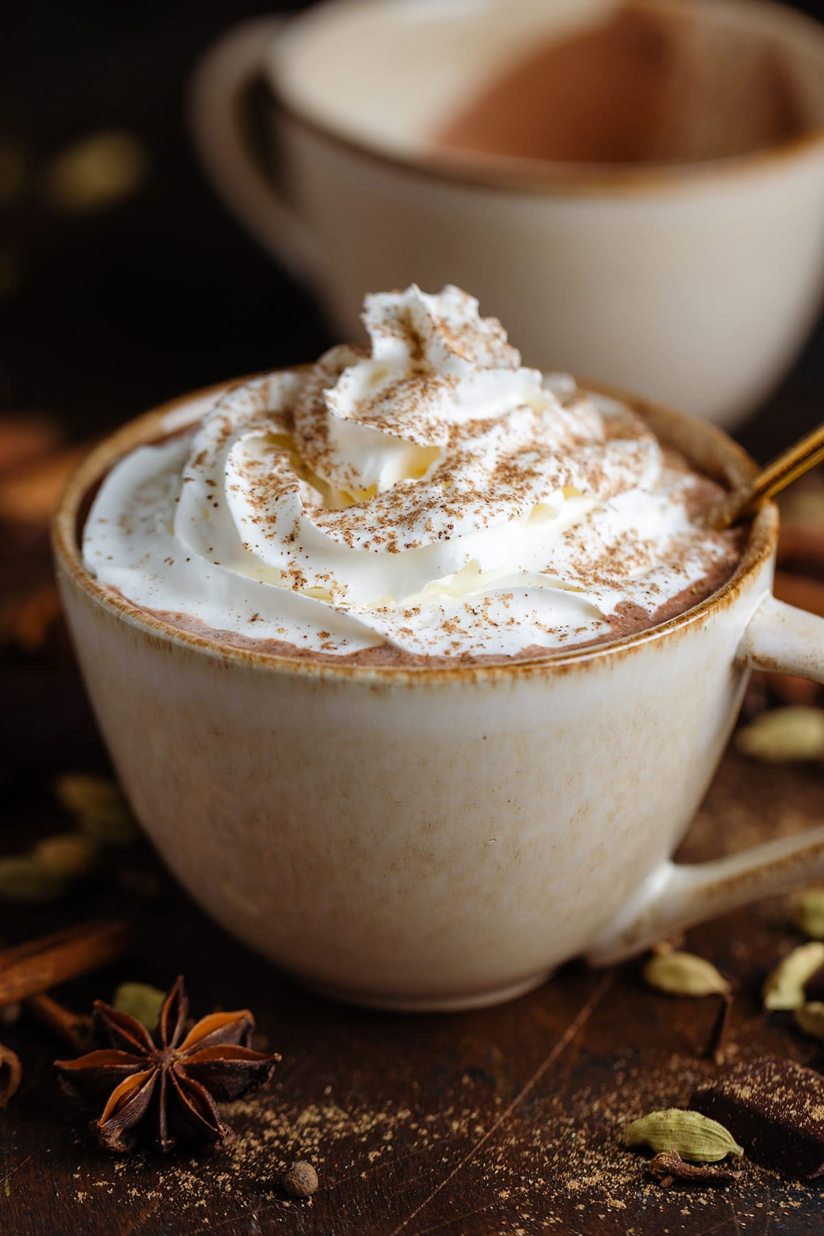 Creamy hot chocolate with whipped cream and chai spice on top in a beige mug.