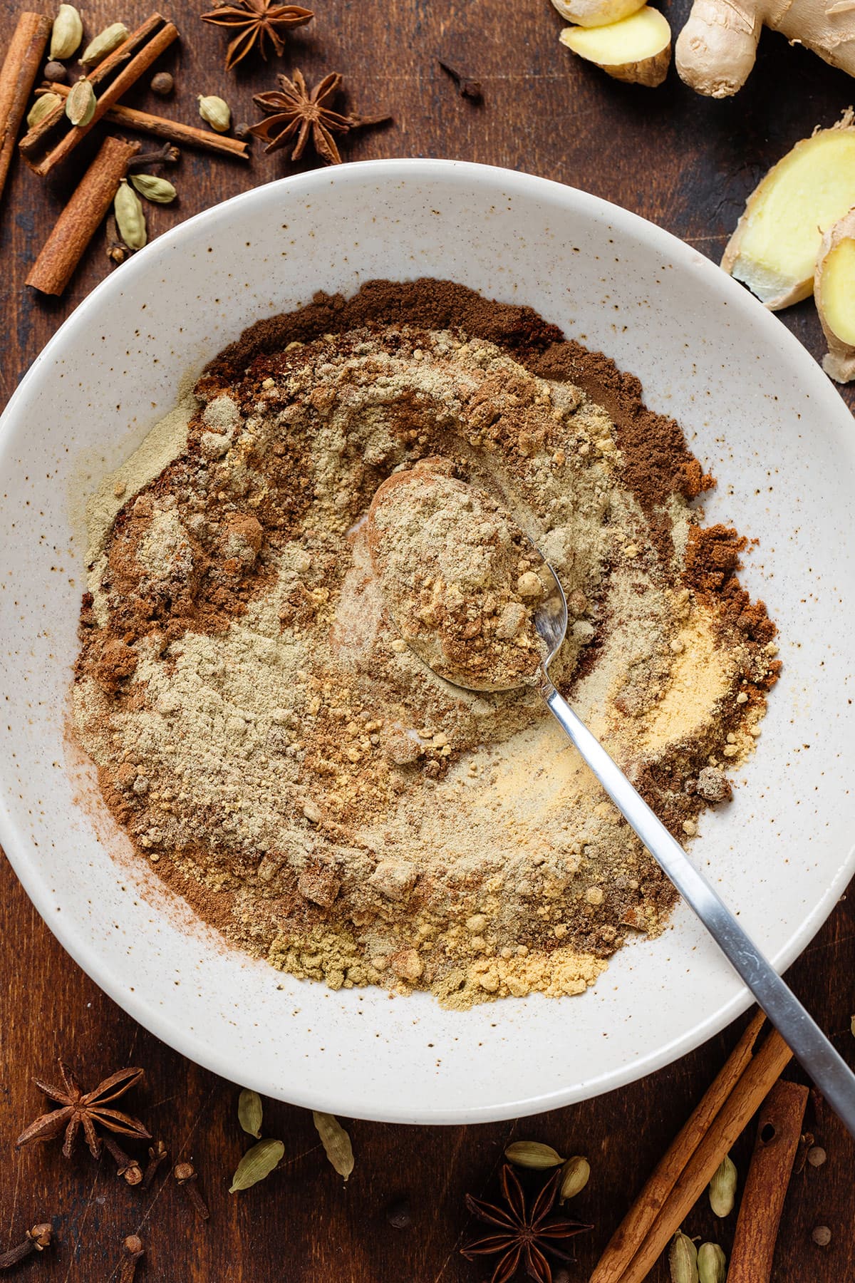 Ground spices in a beige bowl partially stirred together with a silver spoon resting on the side.