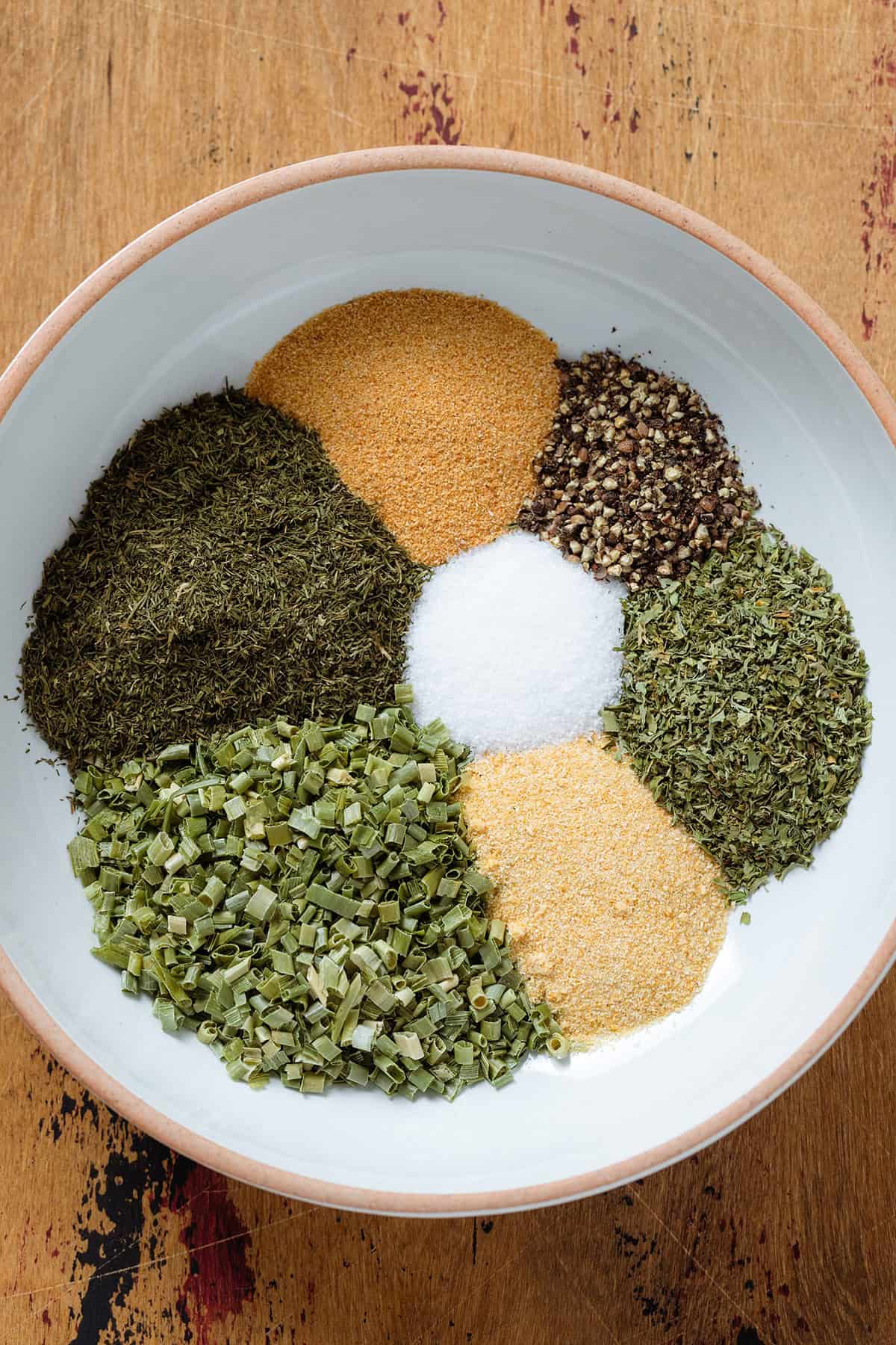 Herbs and spices neatly separated in a white bowl with a beige rim.