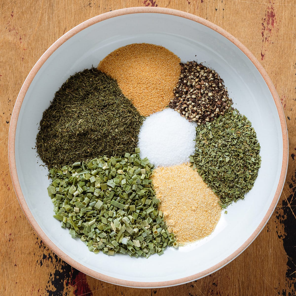 Herbs and spices neatly separated in a white bowl with a beige rim.