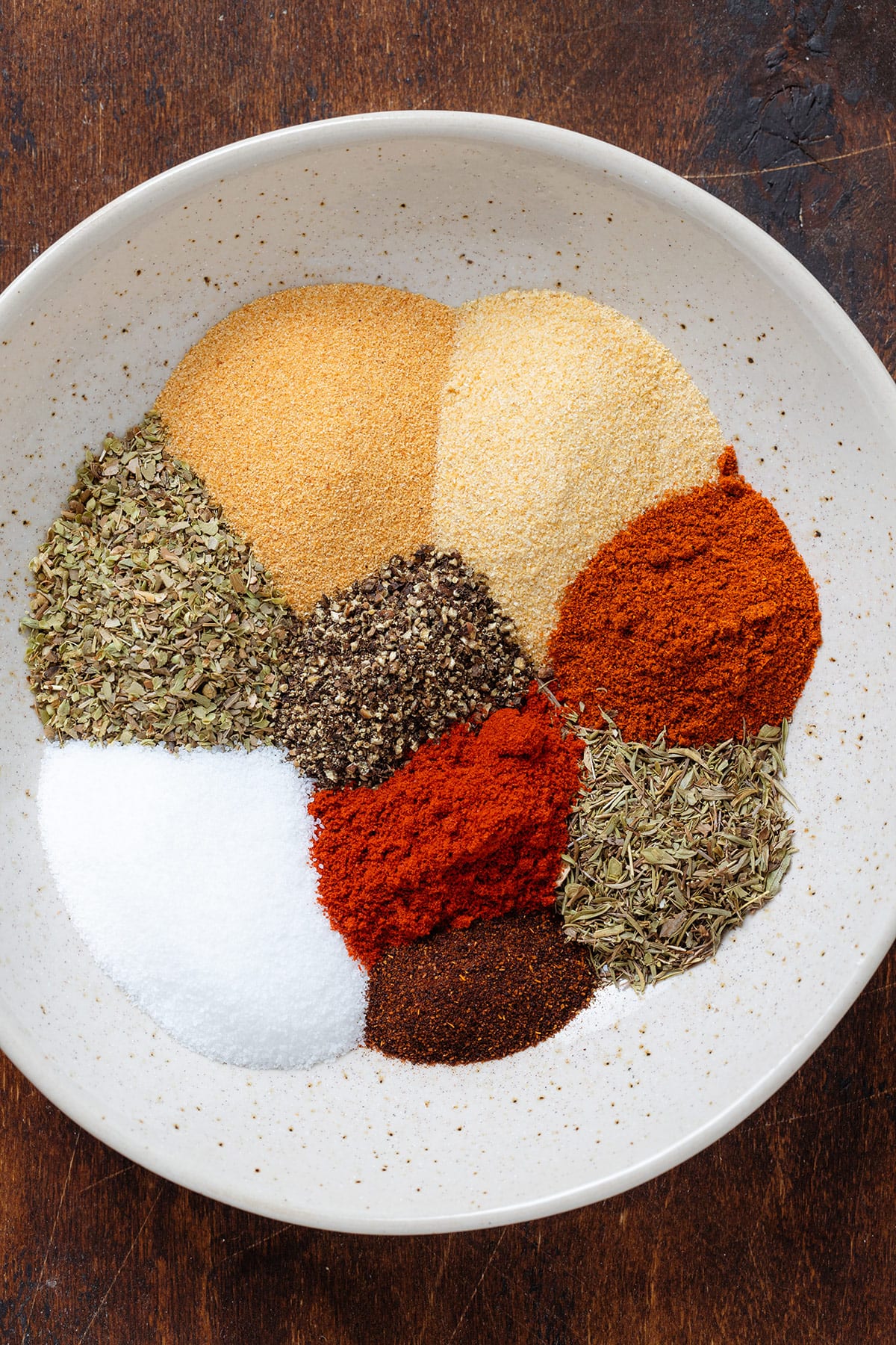Various spices neatly measured out in a beige bowl on a wooden background.