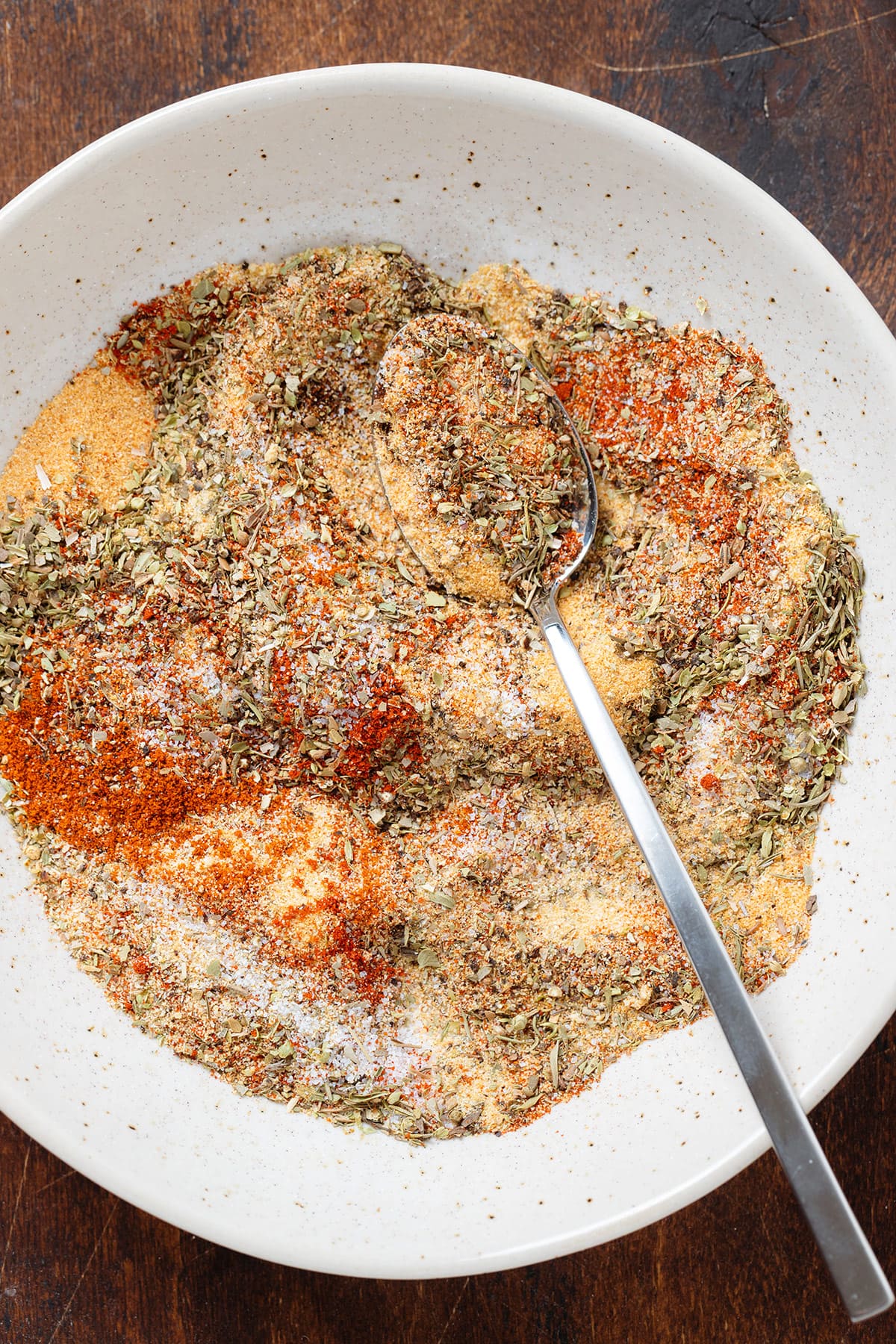 Various spices in a beige bowl being mixed together with a spoon.