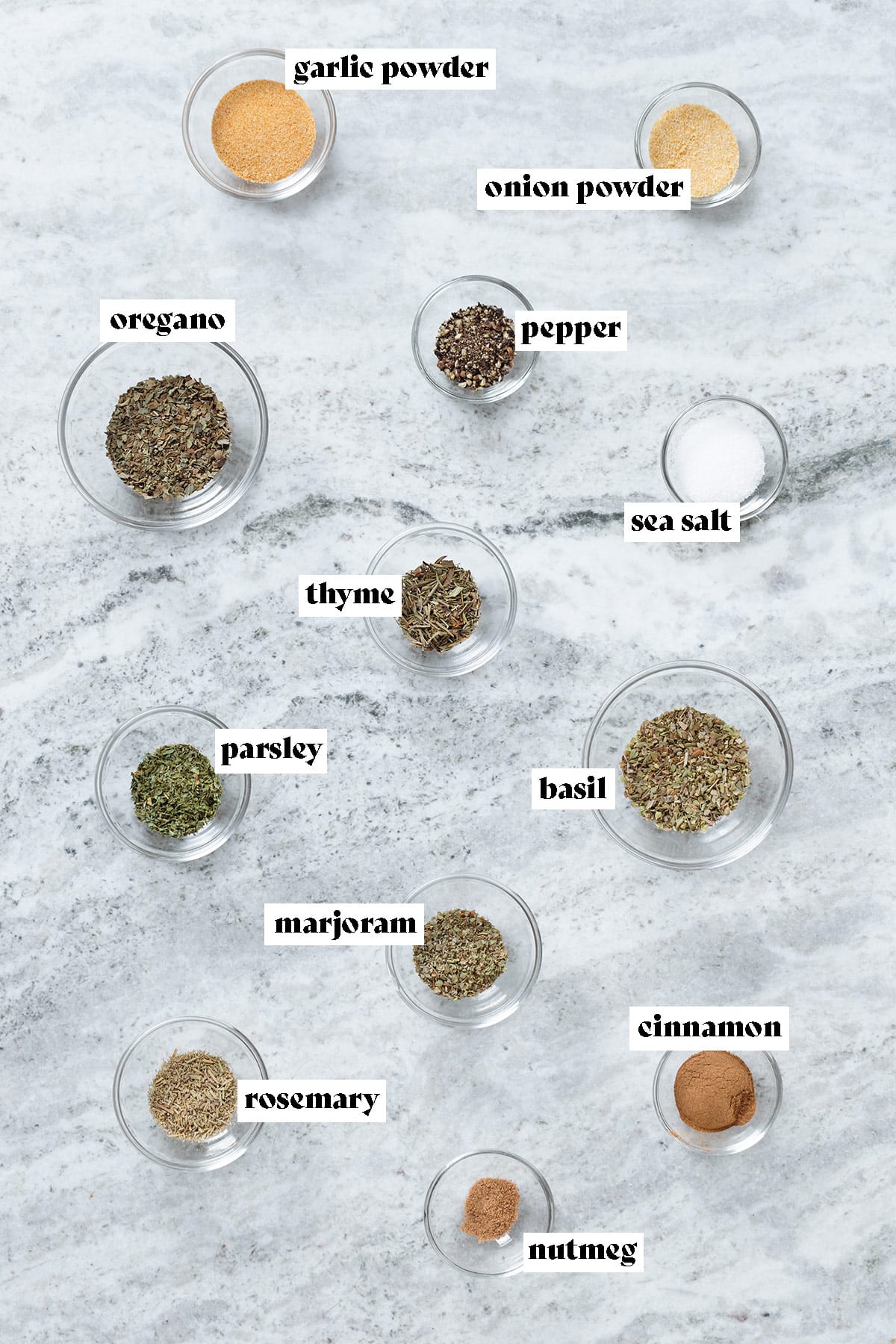Spices and dried herbs measured out in glass bowl on a grey stone background with text overlay.
