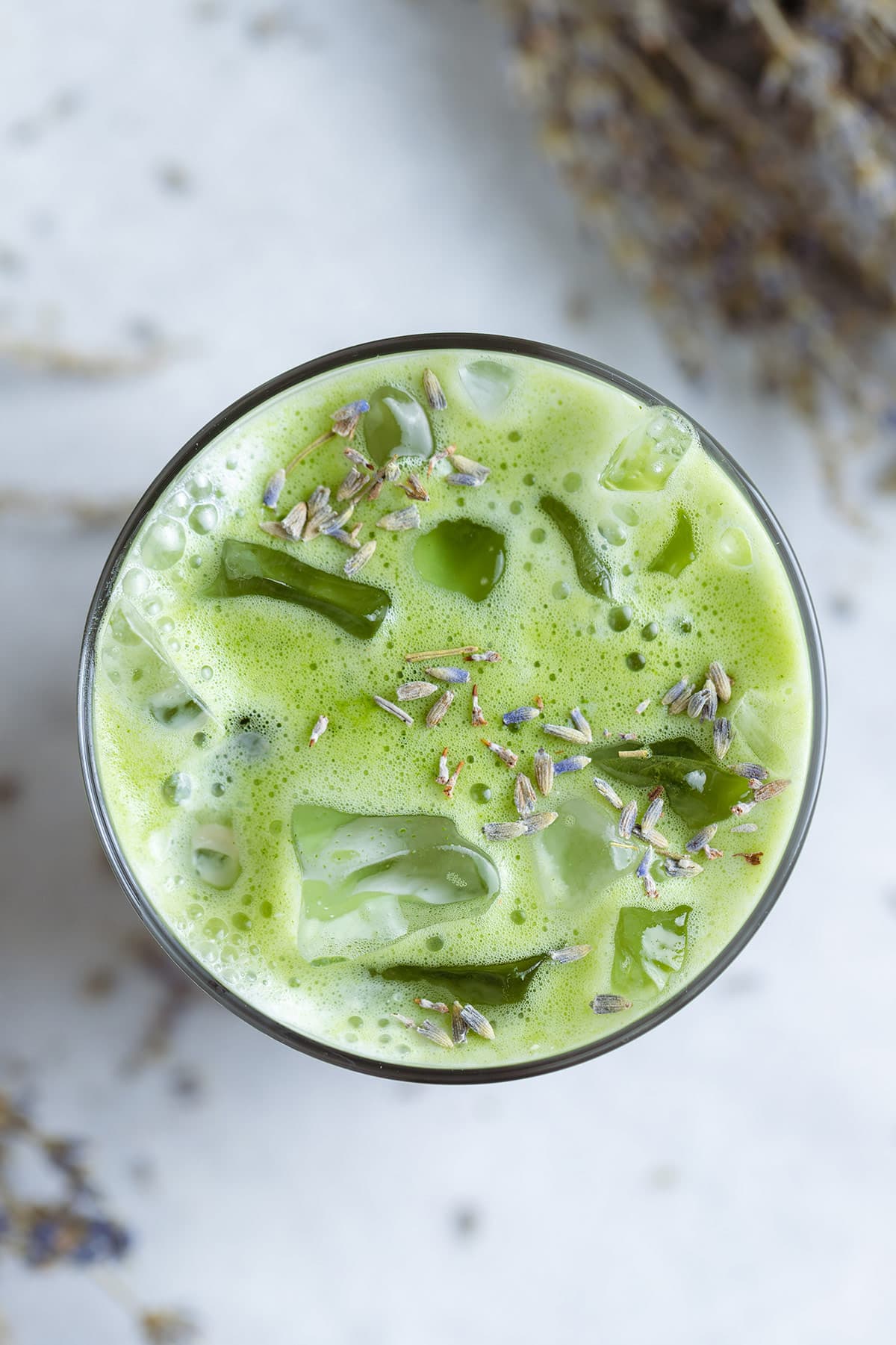Iced matcha latte in a tall glass sprinkled with dried lavender buds.