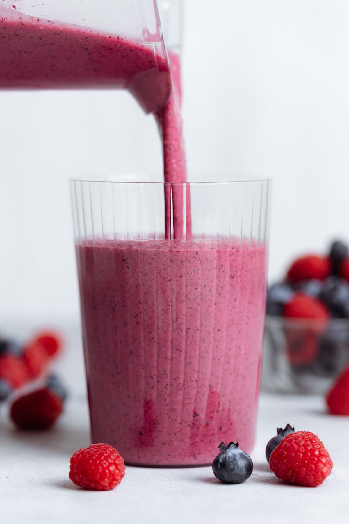 Bright pink smoothie being poured into a tall glass.
