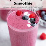 Bright pink smoothie in a tall glass garnished with more berries and a yogurt drizzle.