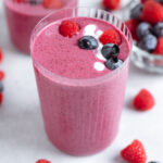 Bright pink smoothie in a tall glass garnished with more berries and a yogurt drizzle.
