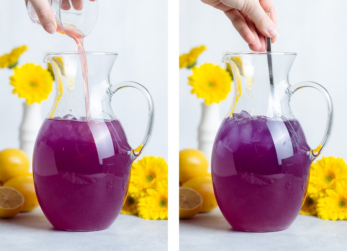Pink syrup being poured into a tall pitcher with dark purple lemonade and the mixture being stirred with a spoon.