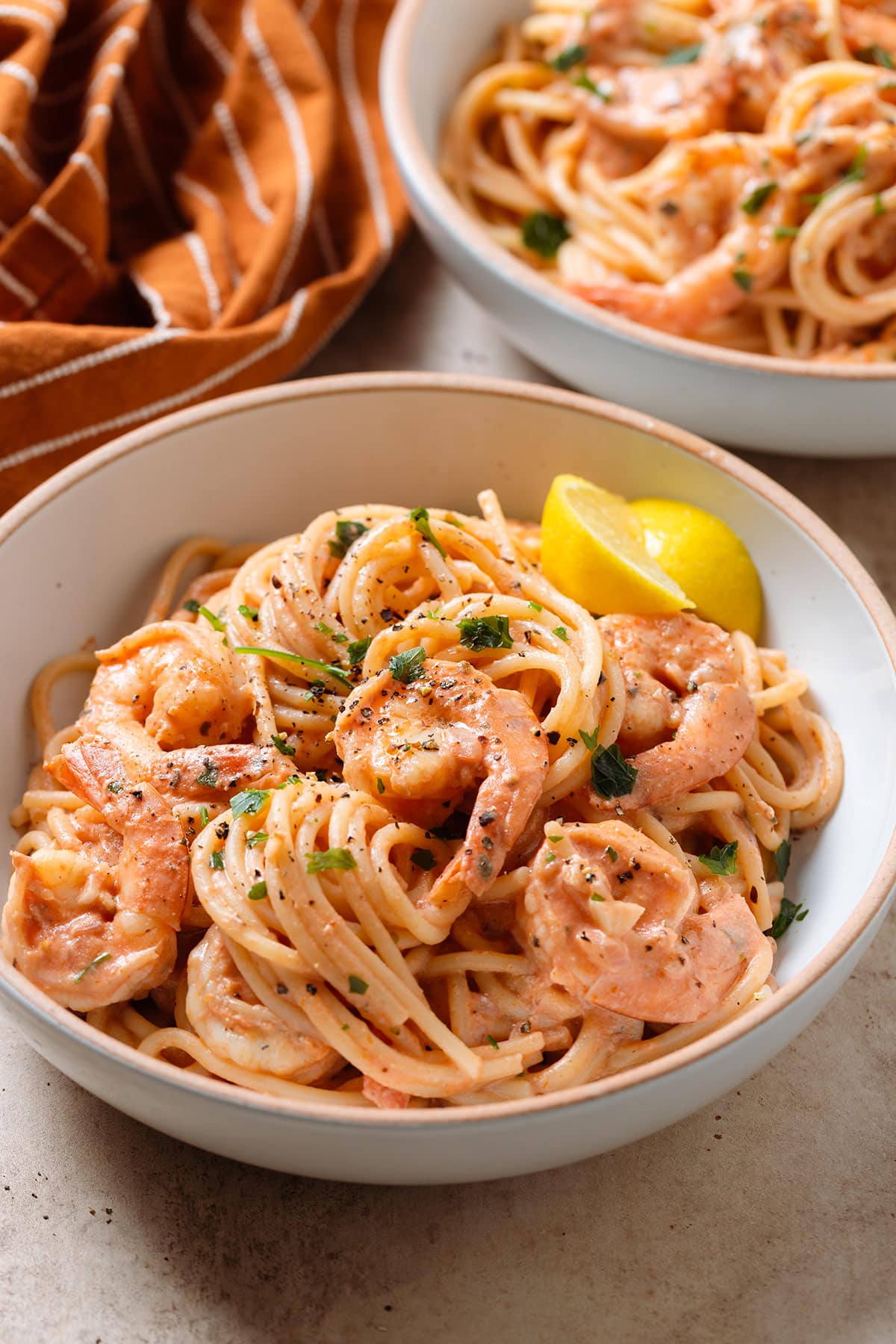 Creamy tomato pasta with shrimp in a low bowl garnished with fresh parsley and two wedges of lemon on the side of the bowl.